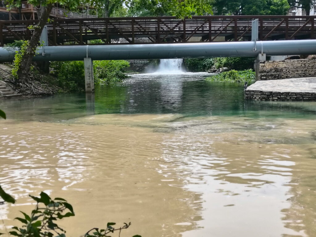 Fresh clear spring water from Comal River waterfall meeting brown storm water runoff from Dry Comal Creek in New Braunfels Texas