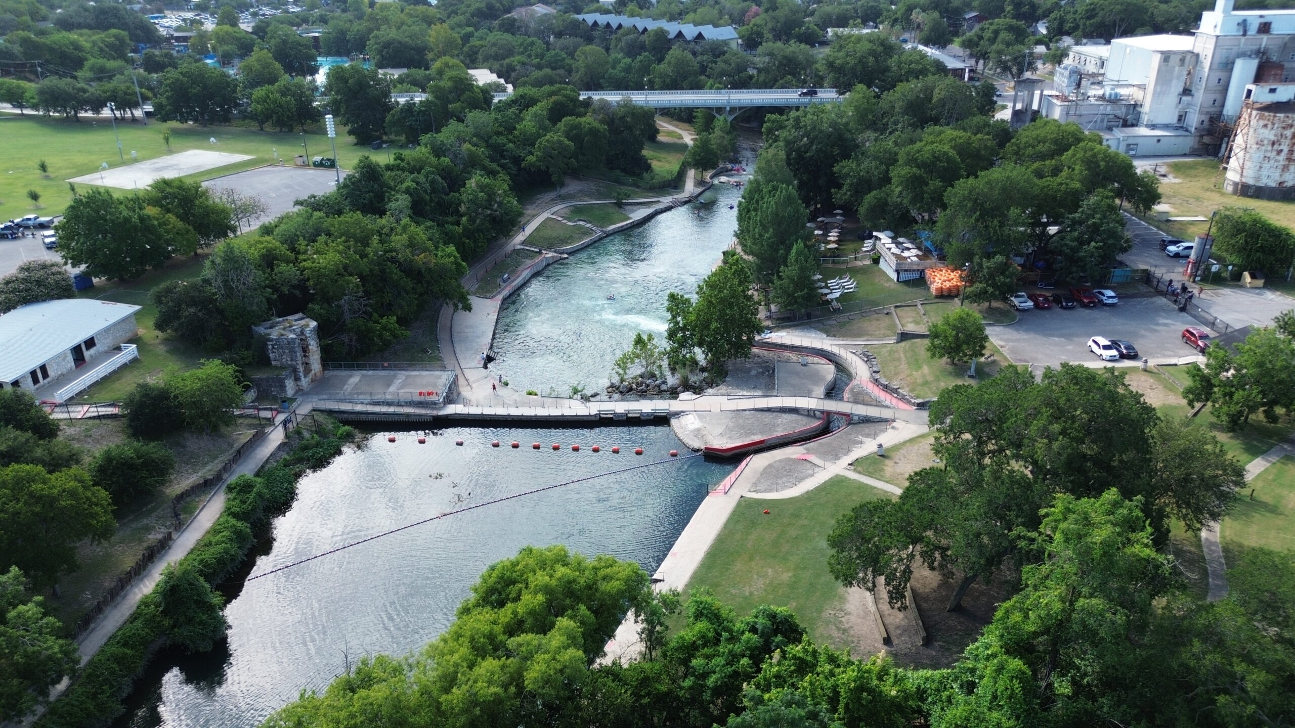 Aerial drone view looking downstream at the Comal River Tube Chute in New Braunfels Texas showing the dam bridge and whitewater exit