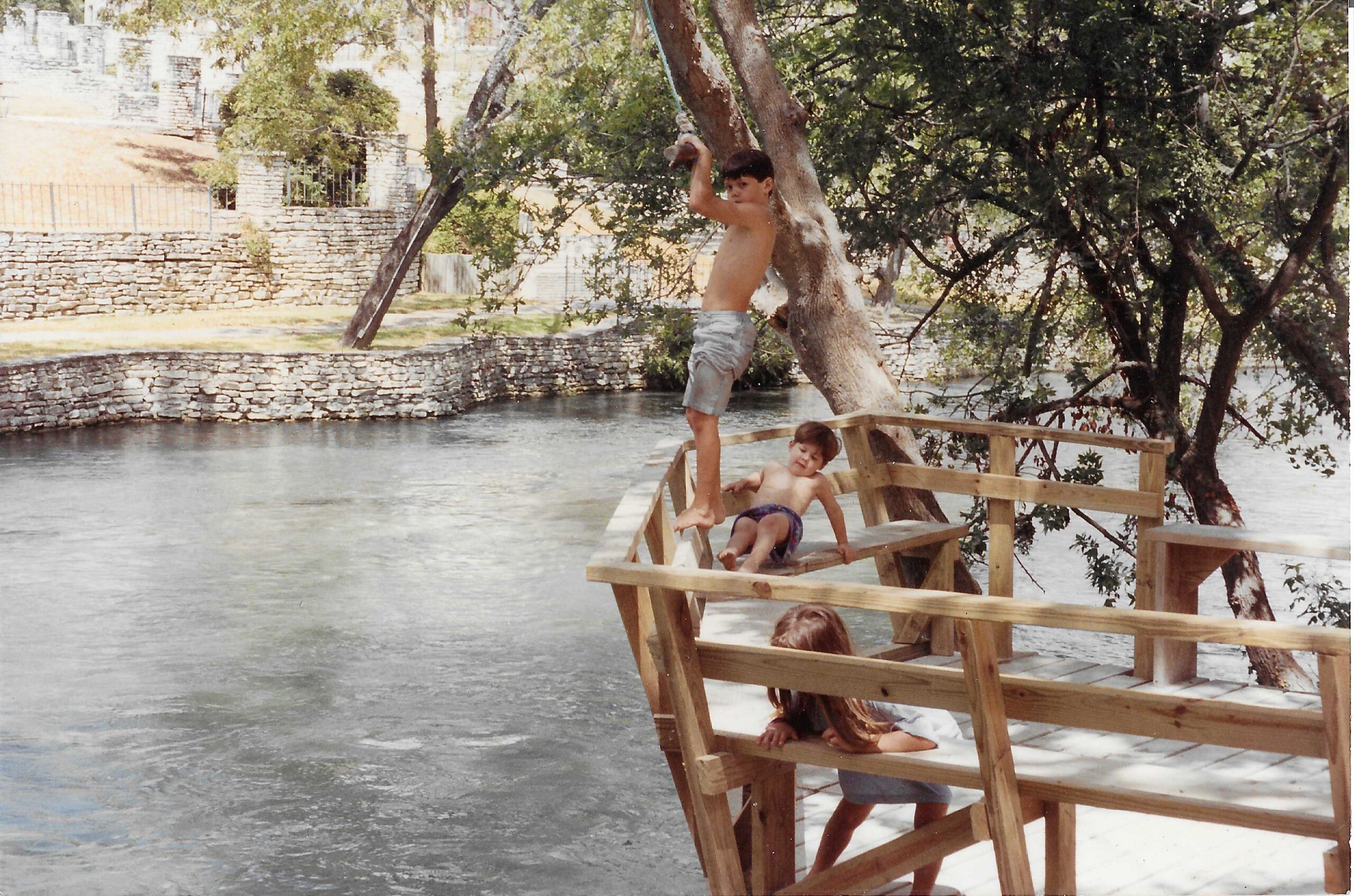 Three children playing on a wooden dock on the Comal River in New Braunfels Texas in the early 1990s at Landa River Trips