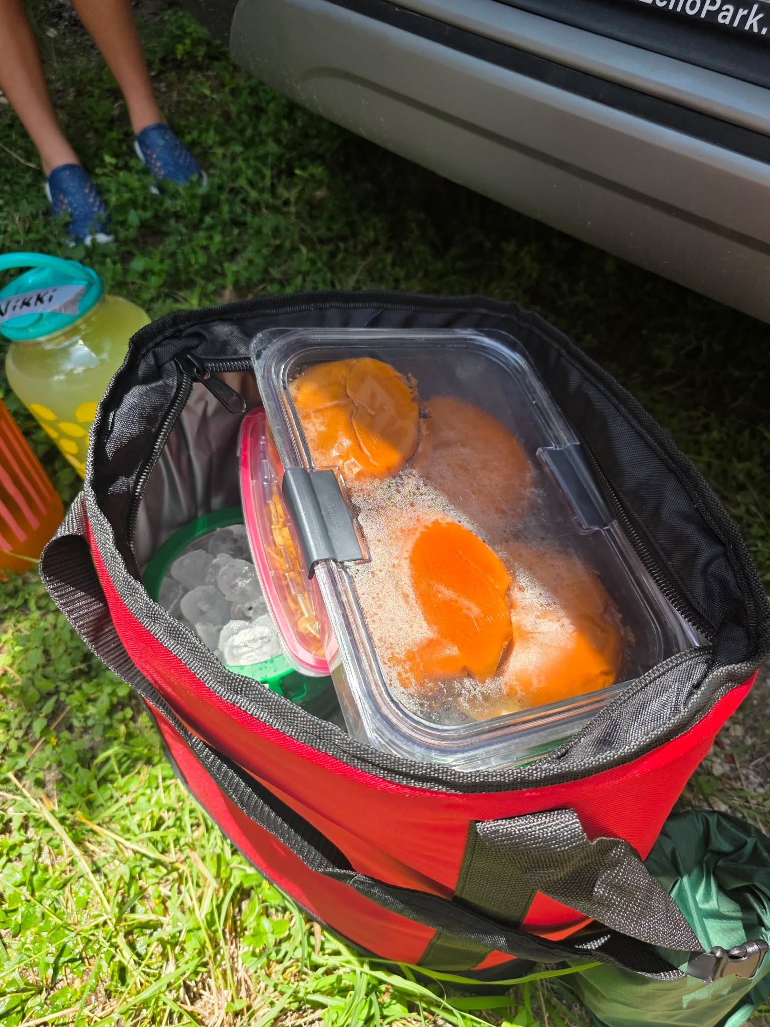 Red soft-side cooler with food in a reusable container and a large jug for pre-mixed drinks for Comal River tubing New Braunfels